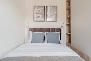 Ein Bett mit Kopfstütze, zwei Kissen, einer Decke und einer Wand mit zwei gerahmten abstrakten Kunstwerken.