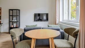 Ein modernes Wohnzimmer mit einem runden Holztisch, grauen Sofas und einem schwarzen Bücherregal.