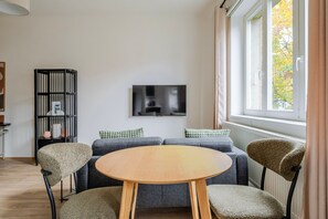 Ein modernes Wohnzimmer mit einem runden Holztisch, grauen Sofas und einem schwarzen Bücherregal.