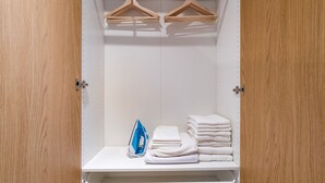 A walk-in closet with wooden doors, a hanging rack, a folded towel stack, and an ironing board. - Blueground | Žižkov, city view, nr Vitkov Hill (PRG-95) (Prague)