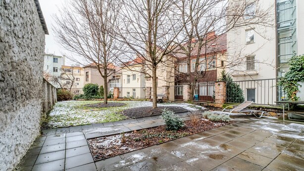 A courtyard with a paved walkway, trees, and a building with multiple windows and balconies. - Blueground | Žižkov, city view, nr Vitkov Hill (PRG-95) (Prague)