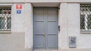 A grey double door with a metal handle, a red and blue sign above it, and a window with metal bars on the left. - Blueground | Žižkov, city view, nr Vitkov Hill (PRG-95) (Prague)