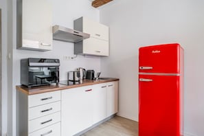 Eine kompakte Küche mit einem roten Kühlschrank, einer Kaffeemaschine und einem Wasserkocher auf der Arbeitsplatte.