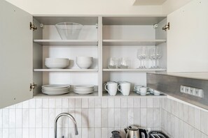 A kitchen with white cabinets, a tiled backsplash, and a stainless steel kettle. - Blueground | Vinohrady, rooftop, nr Riegrovy Sady (PRG-98) (Prague)