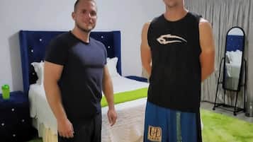 Two men in a room with a bed, a nightstand, and a mirror.