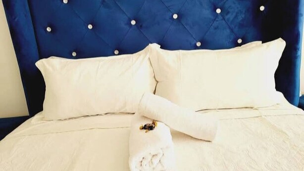 A bed with a tufted headboard, two pillows, and a rolled towel.