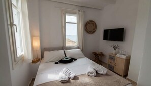 Habitació d'hotel amb llit, televisió, taula de nit, làmpada i vista al mar.