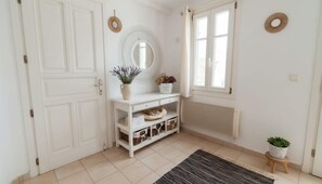 Ein heller Raum mit Tür, Spiegel, Heizkörper, einem kleinen Hocker mit Pflanze und Teppich.