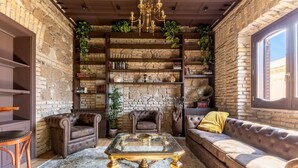 Een knus interieur met een stenen muur, een kroonluchter, leren banken, een glazen salontafel en een boekenplank vol boeken.
