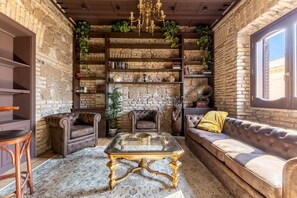 A cozy room with a stone wall, a chandelier, leather sofas, a glass coffee table, and a bookshelf filled with books. - Luxurious, brand new apt Piazza del Popolo 4bedroom and 4bathroom in historic building (Roma)