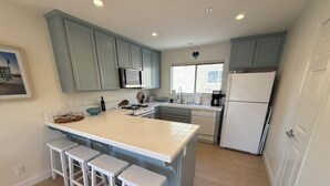 A modern kitchen with a central island, white bar stools, a microwave, and a refrigerator. - NEW LISTING - Coastal Pismo Escape • Steps to Beach & Downtown • 2 Car Garage (Pismo Beach)