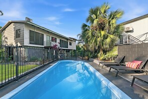 A swimming pool with a fenced area, a house with large windows, and a palm tree.