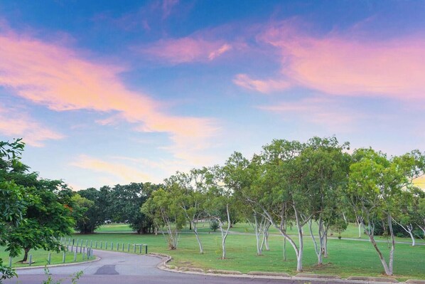 A park with a curved pathway, trees, and a clear sky.