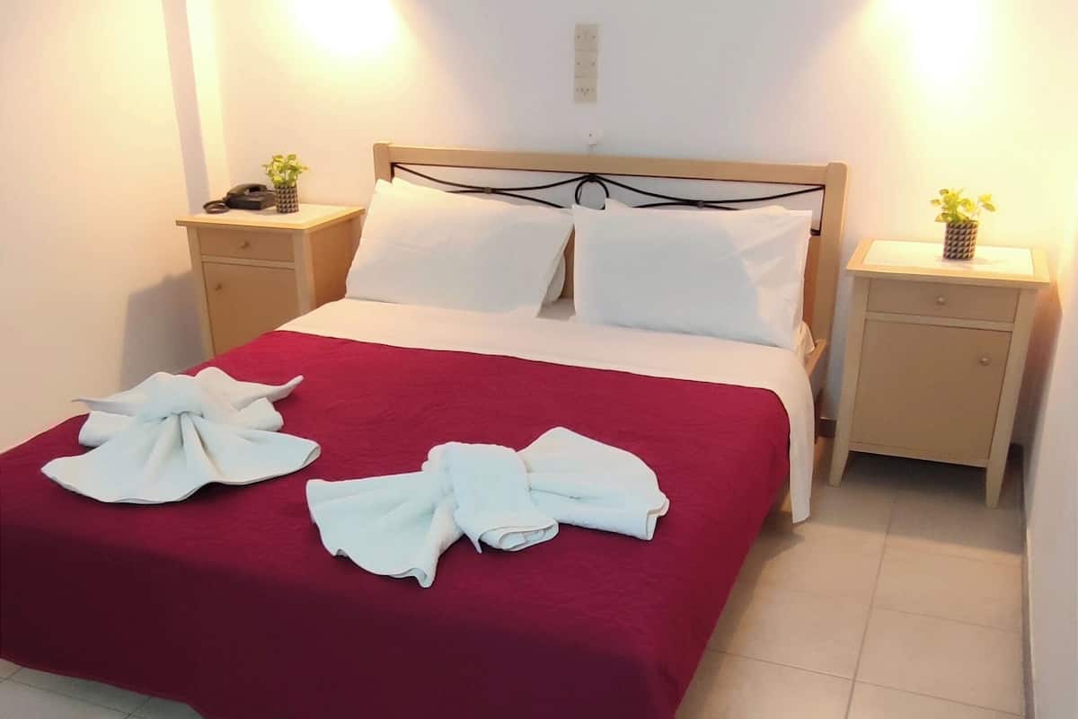 Hotellihuone, jossa on sänky, kaksi yöpöytää ja yksi pienempi sivupöytä.