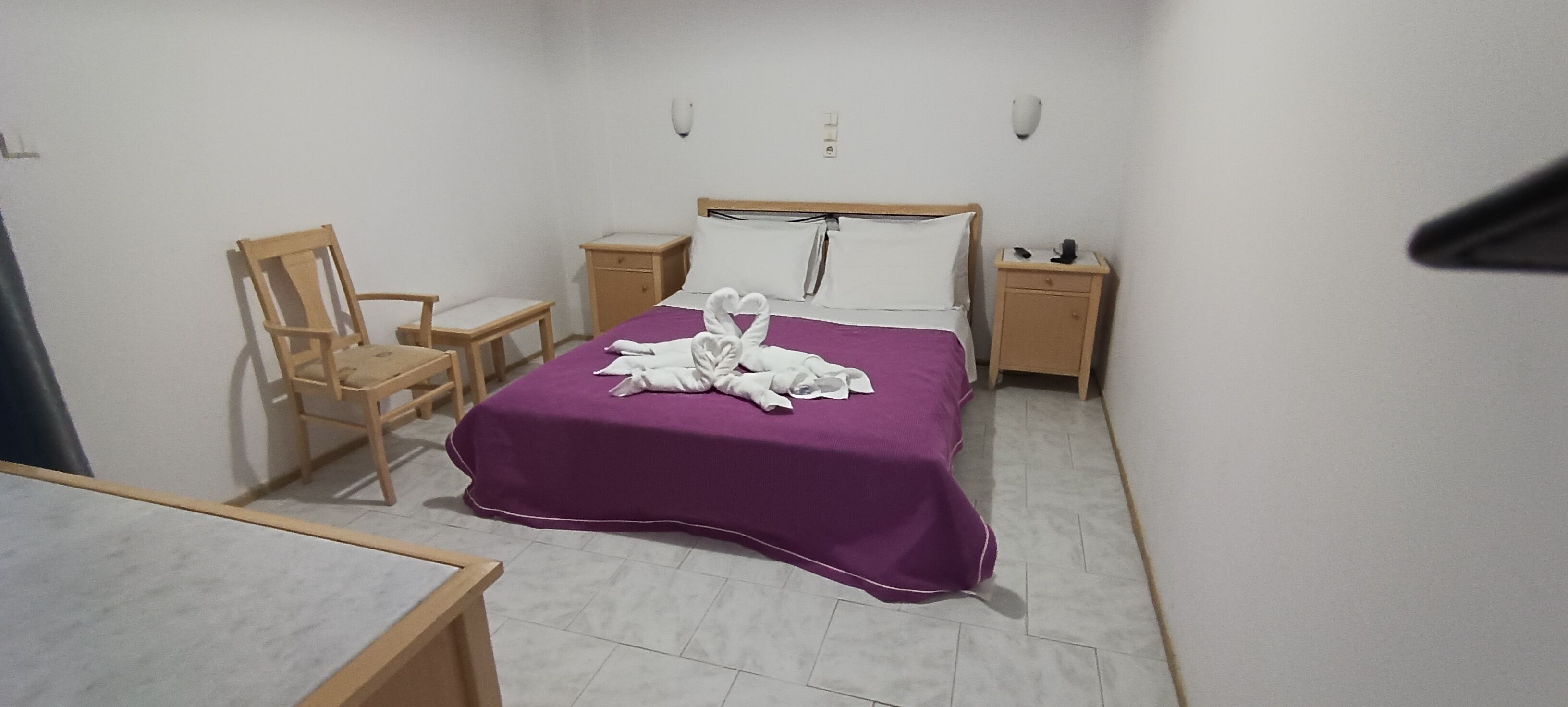 A hotel room with a bed, a chair, a small table, and a nightstand.