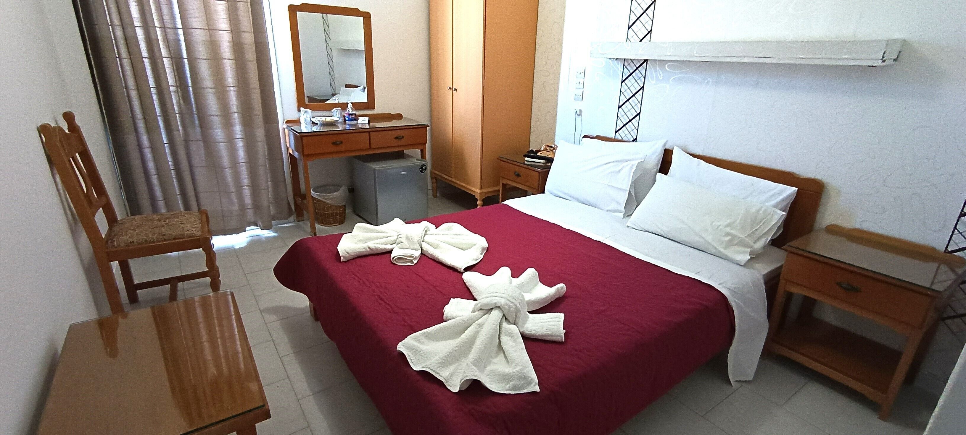 A hotel room with a bed, a desk, a chair, a wardrobe, and a mirror.