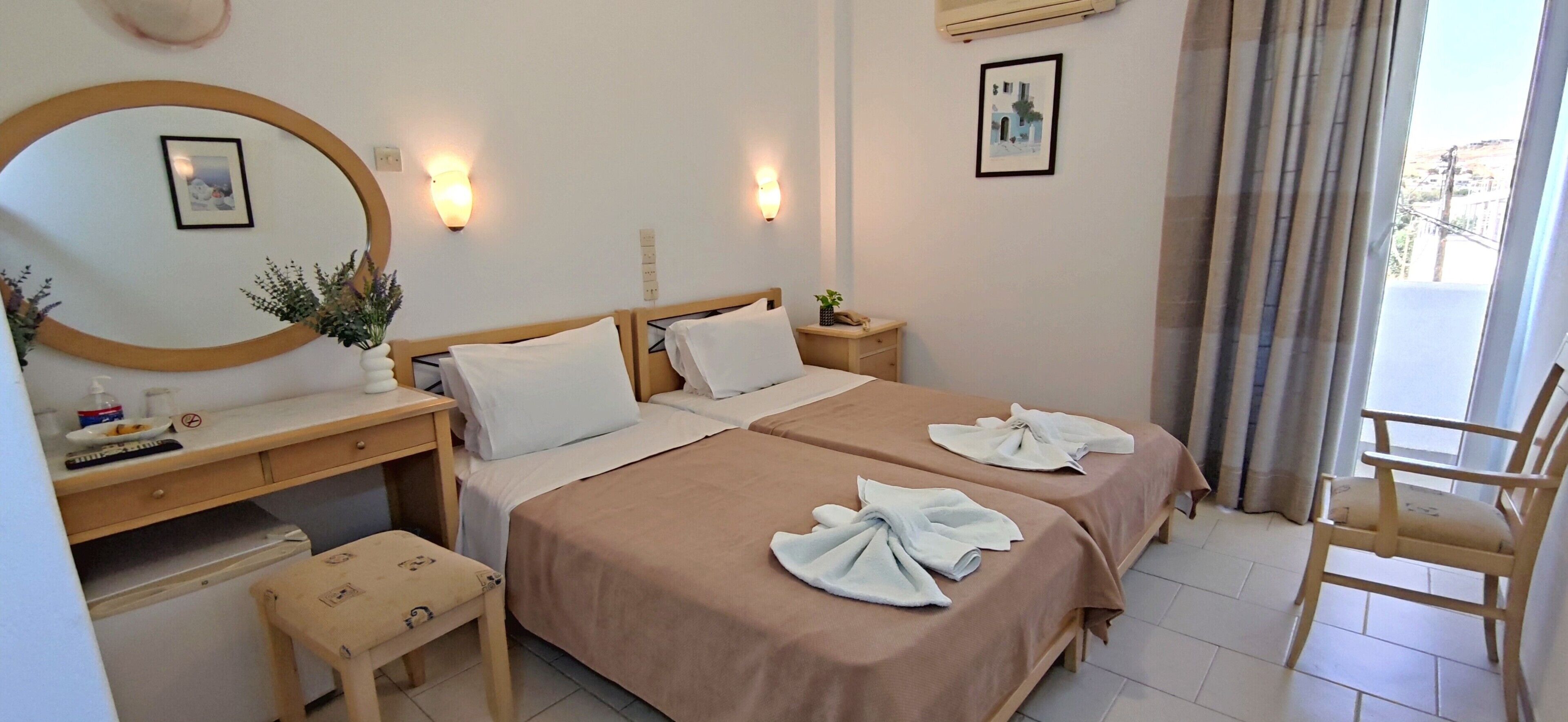A hotel room with two beds, a desk, a chair, a small table, and a window with curtains.