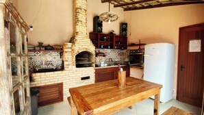 A kitchen with a brick oven, wooden table, and tiled backsplash. - Flamboyant Space - Armação dos Búzios - Summer House Near the Beach (Armação dos Búzios)