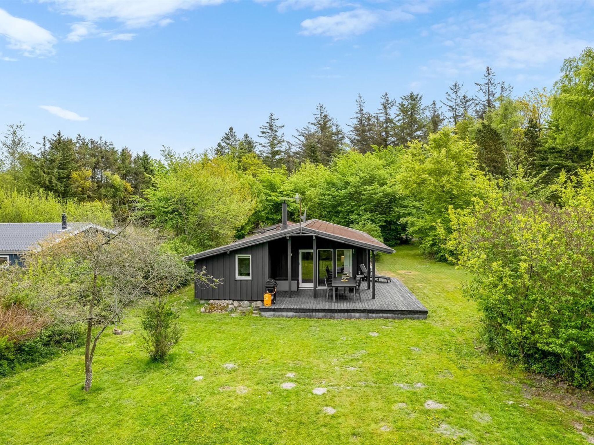 Une petite cabane dotée d’une terrasse, entourée d’une végétation luxuriante et d’arbres.