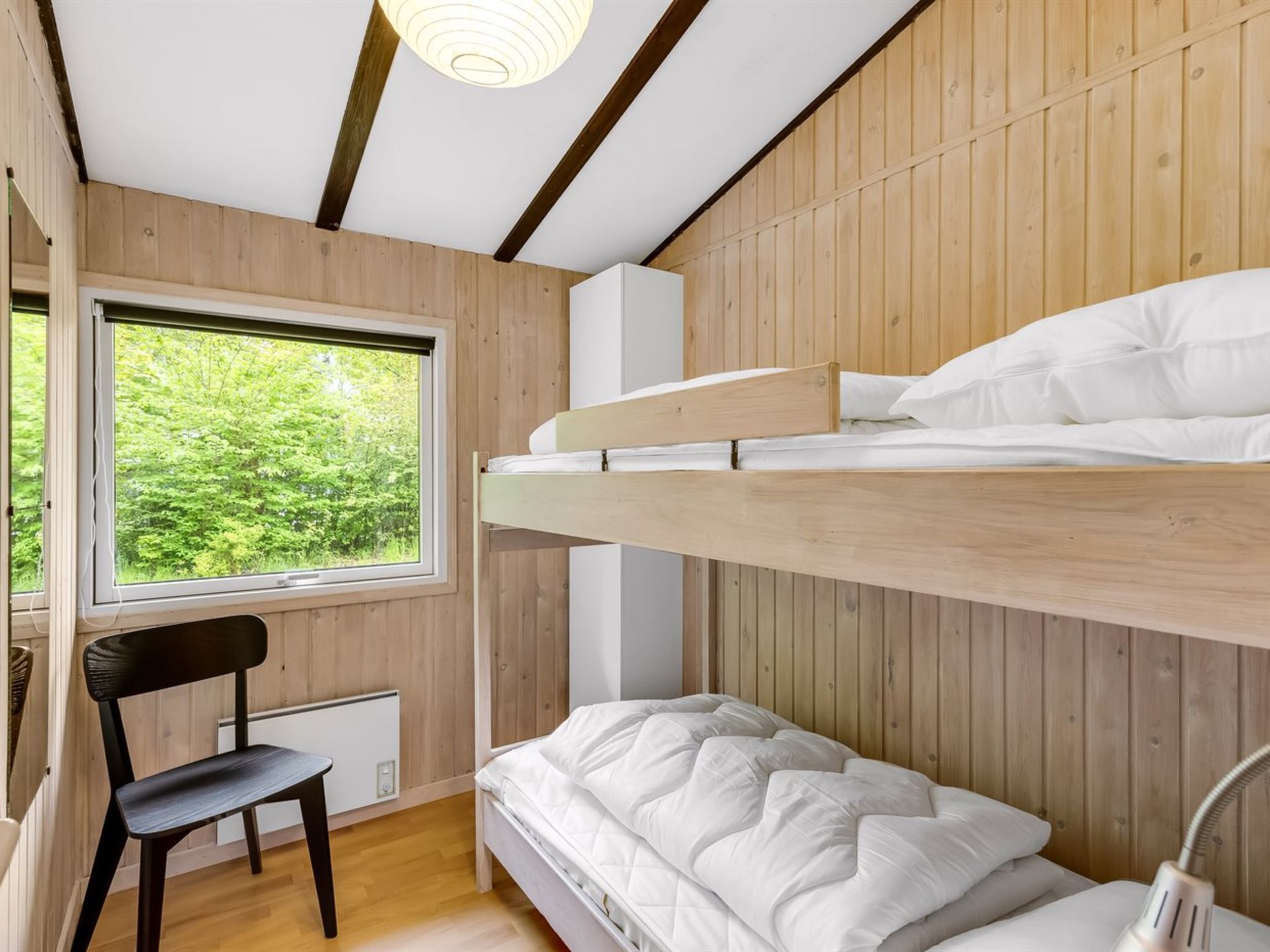 Une chambre avec un lit superposé, une fenêtre, une chaise et un radiateur.
