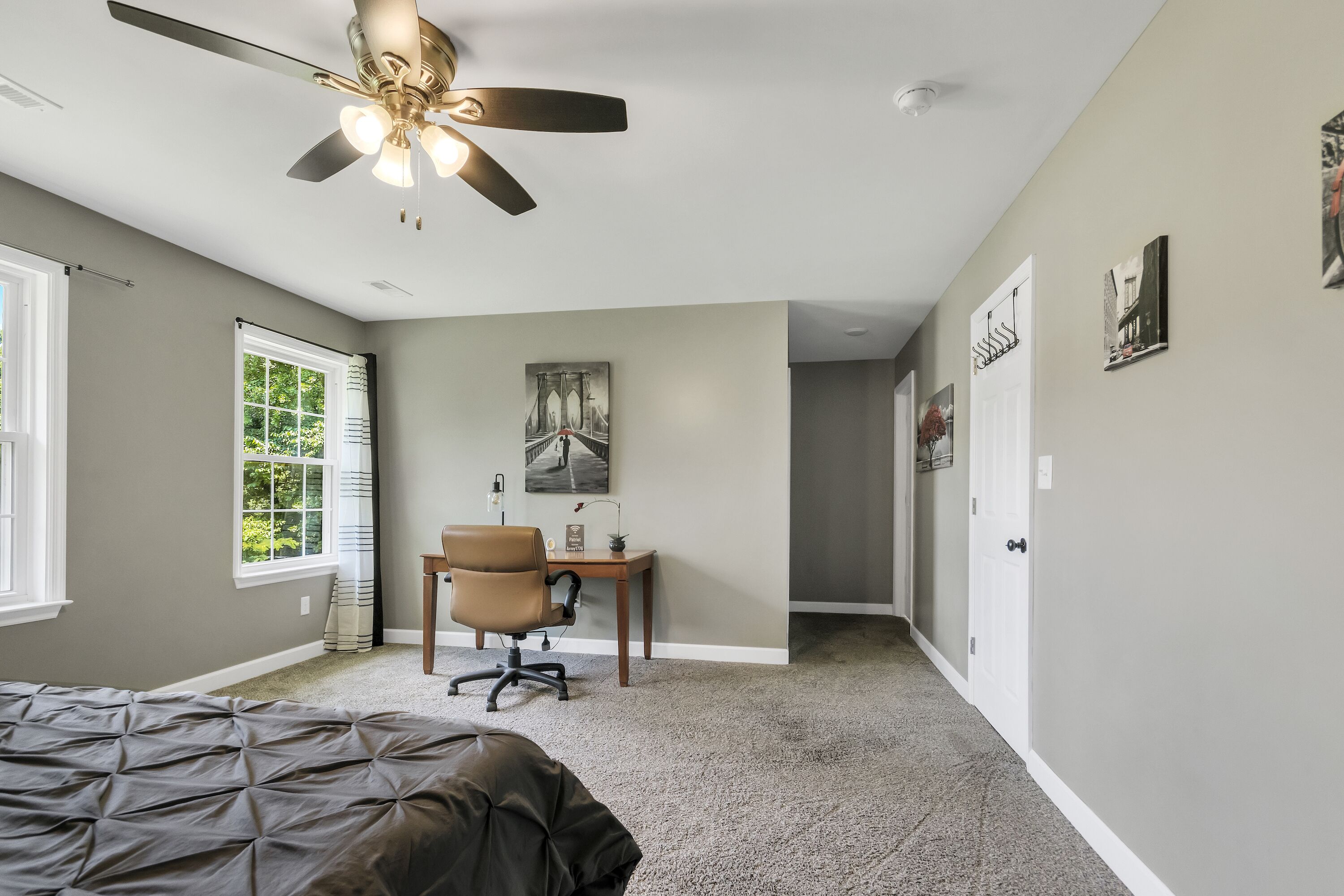 A bedroom with a bed, a desk, a chair, a ceiling fan, and a window.