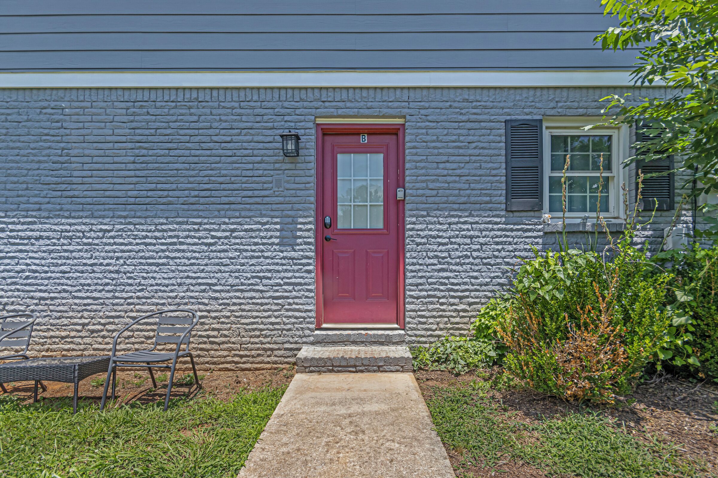 A house with a red door, a small porch with a chair, and a window with shutters.