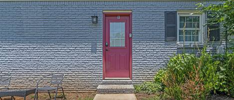 A house with a red door, a small porch with a chair, and a window with shutters.
