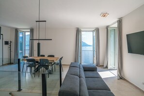 A modern living room with a sofa, dining table, chairs, and a TV. - Sant' Anna Deluxe, Menaggio (Nobiallo), Italy (Menaggio (Nobiallo))