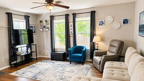 A living room with a flat-screen TV, a ceiling fan, a blue armchair, a beige sofa, and a wooden floor. - Cozy Coastal House Near Fishing, Bay Views (Palacios)