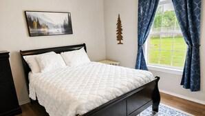 A bedroom with a bed, a nightstand, a window with curtains, a wall-mounted picture, and a small wooden tree decoration. - Cozy Coastal House Near Fishing, Bay Views (Palacios)