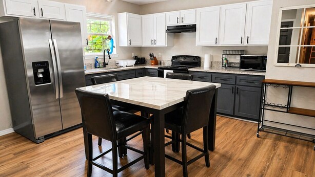 A modern kitchen with a stainless steel refrigerator, a dining table with chairs, and white cabinetry. - Cozy Coastal House Near Fishing, Bay Views (Palacios)