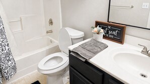 A bathroom with a toilet, sink, and bathtub. There is a framed sign on the wall and a towel on the counter. - Cozy Coastal House Near Fishing, Bay Views (Palacios)