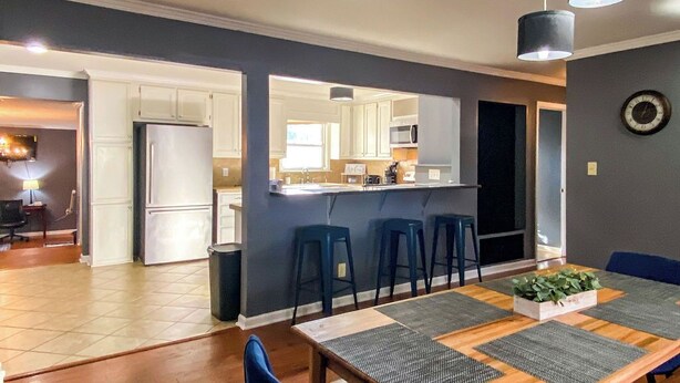 Una cocina moderna con armarios blancos, un refrigerador y un comedor con mesa de madera y sillas azules.