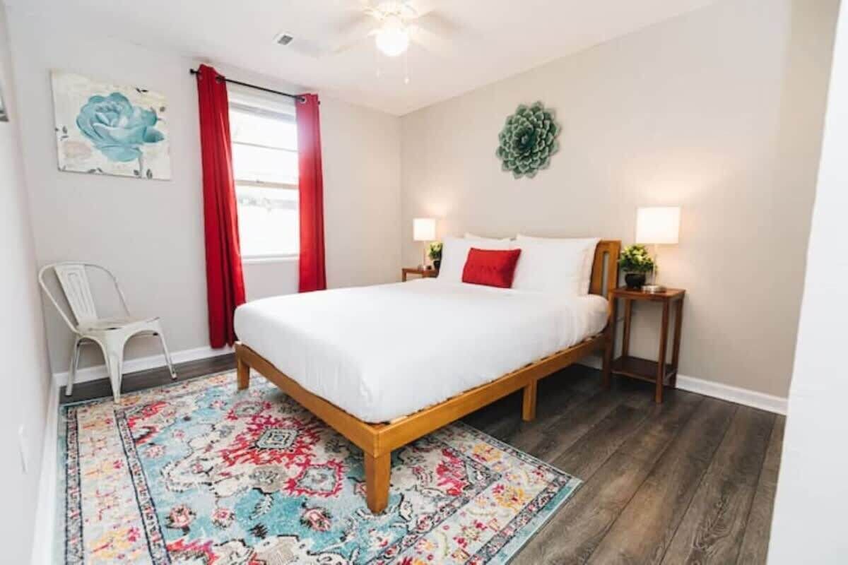 Une chambre à coucher avec un lit en bois, des rideaux rouges, un tapis à motifs floraux et une petite table de chevet avec une lampe.