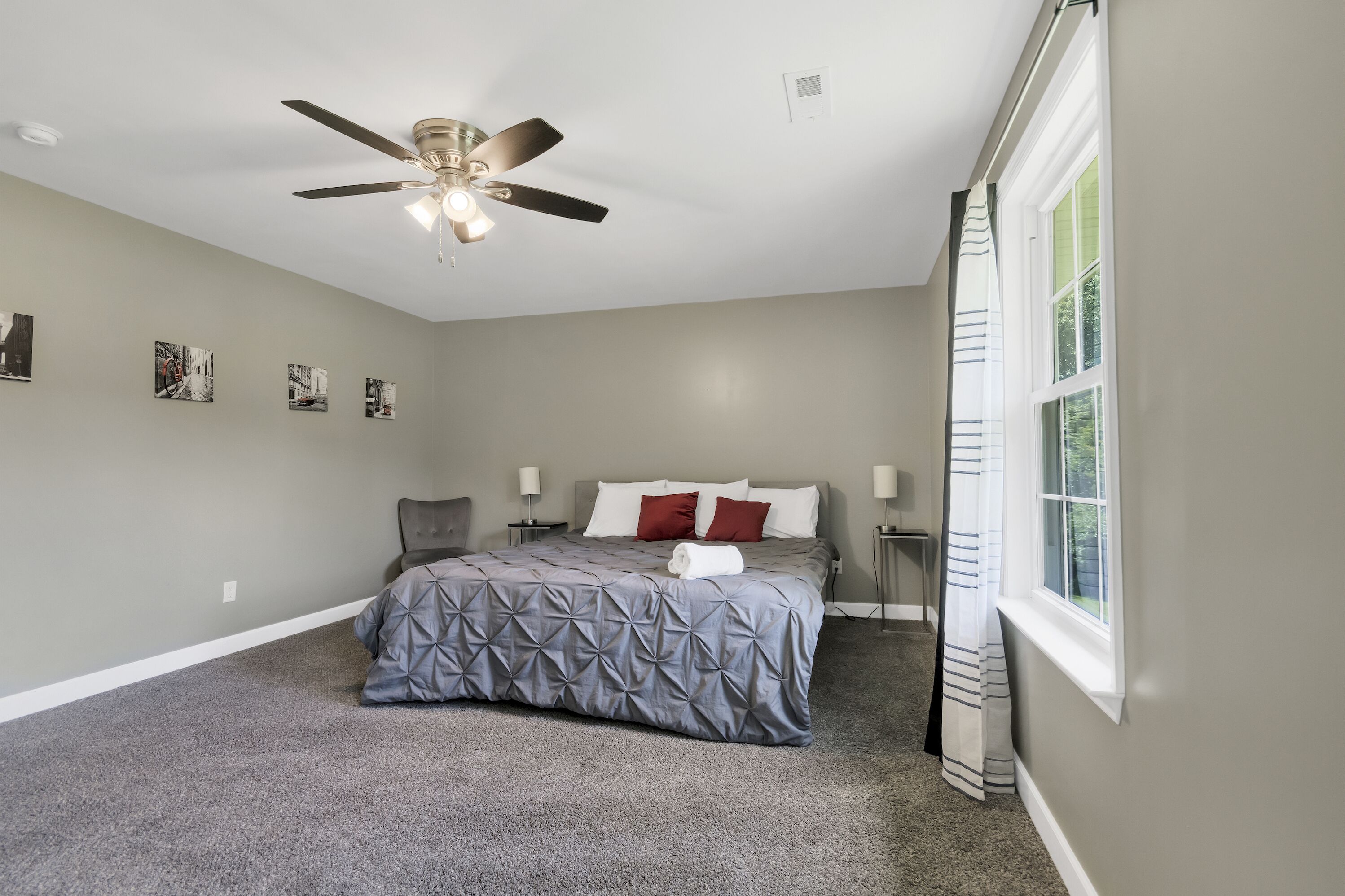 A bedroom with a bed, a ceiling fan, a window, and wall-mounted artwork.