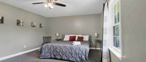 A bedroom with a bed, a ceiling fan, a window, and wall-mounted artwork.