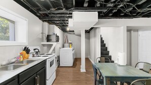 A kitchen with a sink, stove, and refrigerator; a dining area with a table and chairs; and a staircase leading to another level.