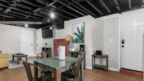A dining area with a table, chairs, a lamp, and a brick wall.