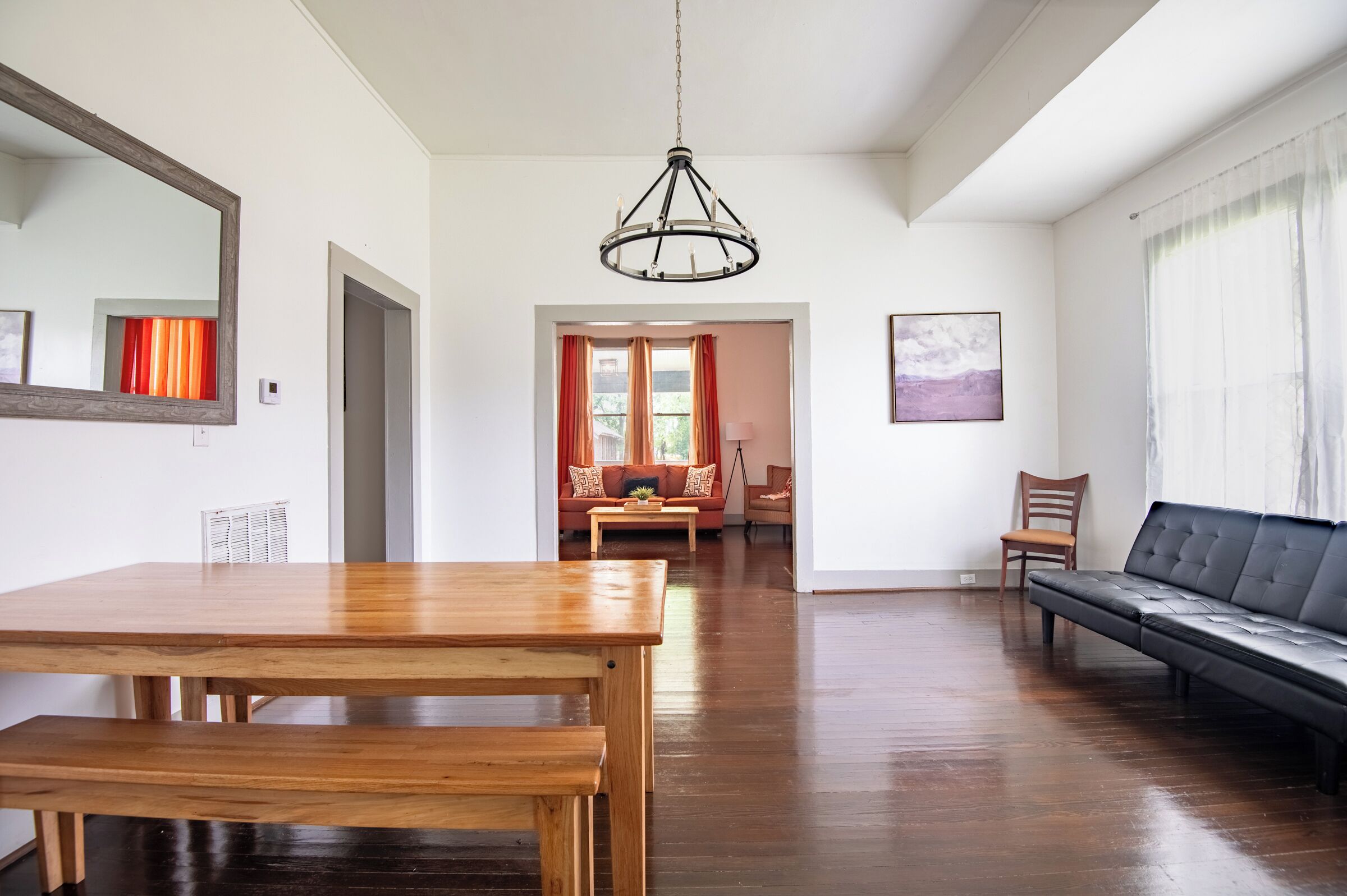 A spacious room with a wooden dining table, a black leather sofa, and a chandelier.