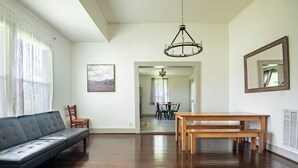 Una habitación amplia con sofá, banco de madera, una araña y un área de comedor al fondo.