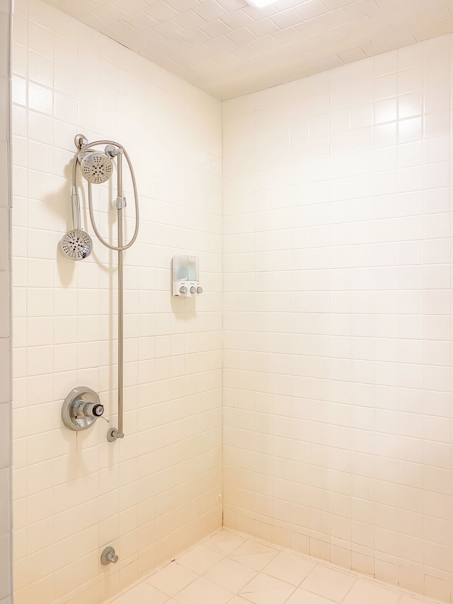 Een badkamer met witte betegelde wanden, een douche met een handdouche en bedieningspaneel aan de muur.