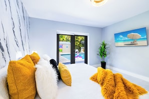 Ein Schlafzimmer mit Bett, großem Fenster, einer Pflanze und einem Bild an der Wand.