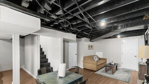 A dining area with a table and chairs, a staircase, a sofa, and a lamp. - Garden Bungalow at Broadmoor -WiFi/Parking/Cozy (Birmingham)
