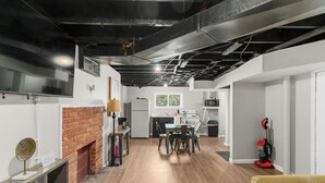 A modern kitchen with a brick fireplace, a dining area with chairs, and a yellow sofa. - Garden Bungalow at Broadmoor -WiFi/Parking/Cozy (Birmingham)