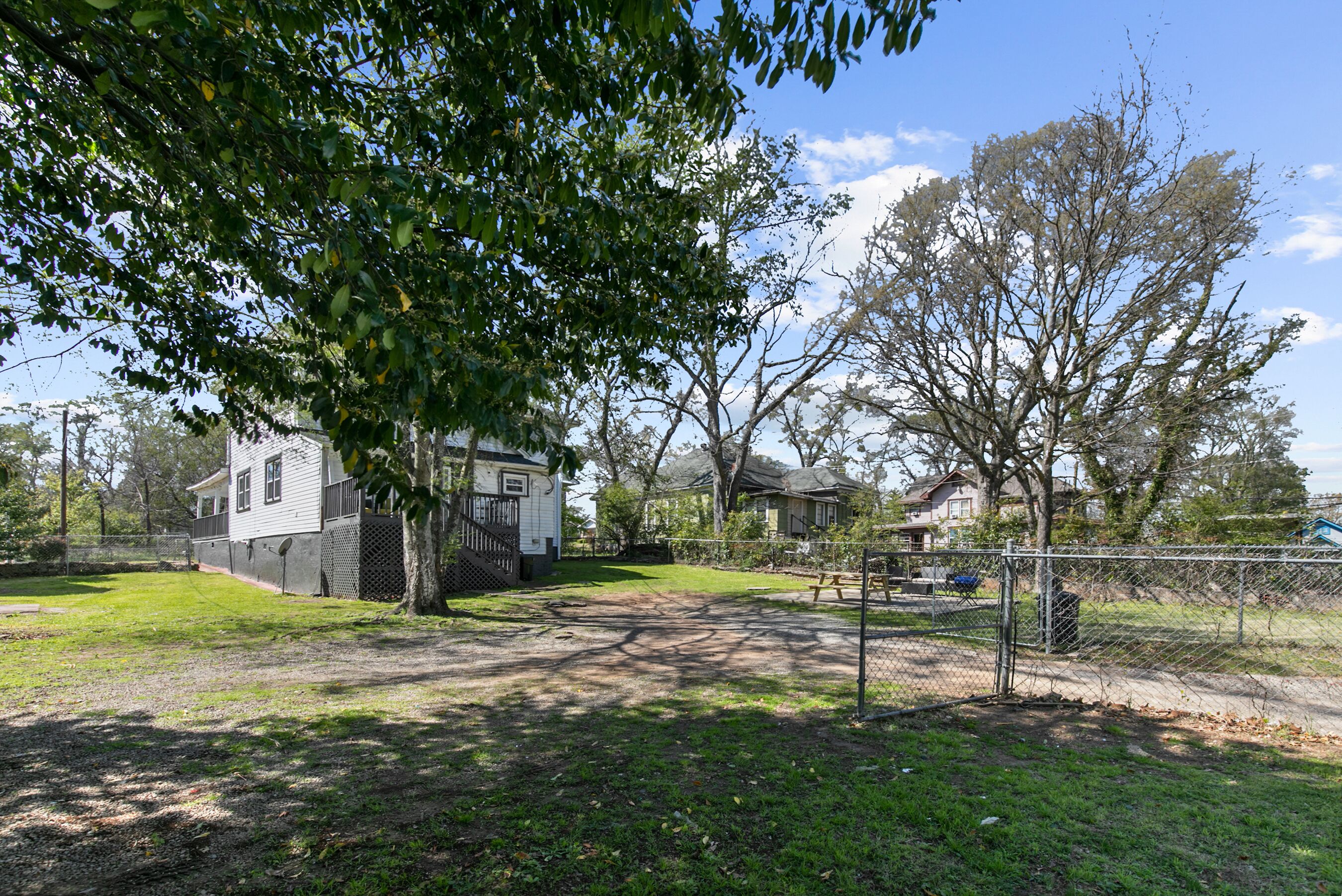 A fenced yard with a picnic table, a tree, and houses in the background.