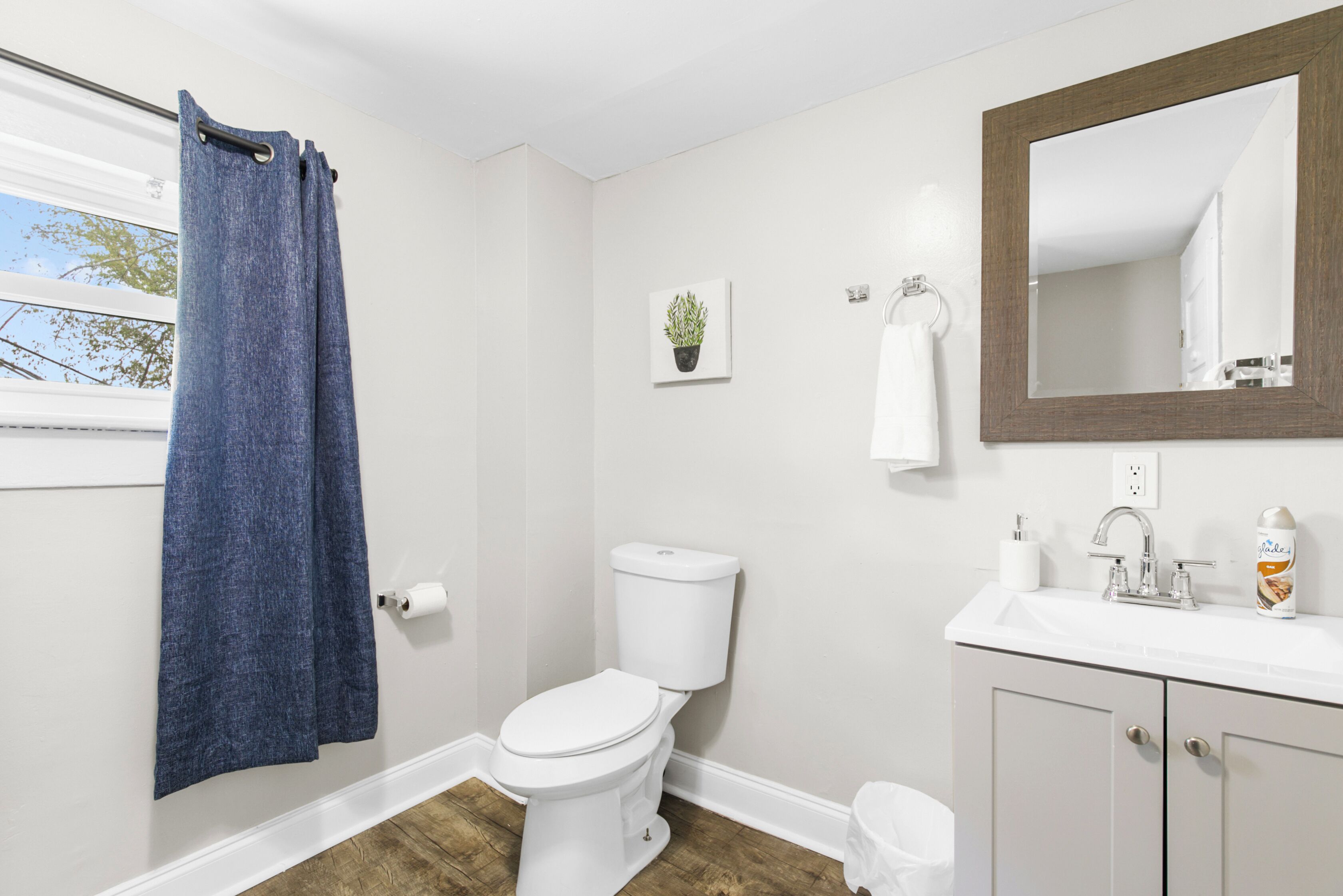 Un baño con inodoro, lavabo, espejo, toallero y una ventana con cortinas.