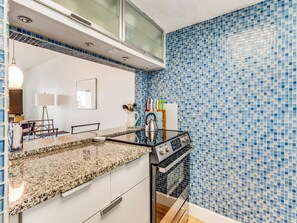 A kitchen with a granite countertop, stainless steel appliances, and blue mosaic tiles. - Bent Palm 302 (Ormond Beach)