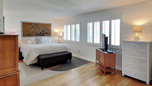 Quarto com cama, abajures, penteadeira, televisão e janela com persianas.