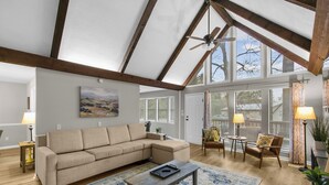 A spacious living room with a high ceiling, a sectional sofa, a coffee table, and a view through large windows. - Lake View Landing | Pool/Groups/Nature/Games (Birmingham)