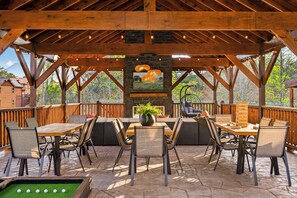 A covered outdoor seating area with a wooden table and chairs, a stone fireplace, and a view of the surrounding landscape. - Bethlehem Lodge (Sevierville)